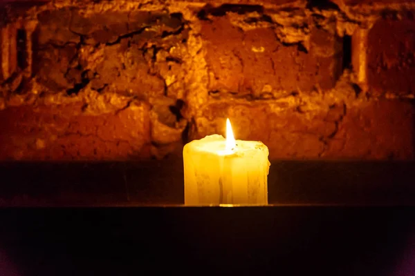 Свеча горит на фоне старой кирпичной стены — стоковое фото
