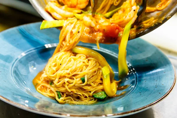 De kok zet de pasta met de groenten en garnalen op een pla — Stockfoto