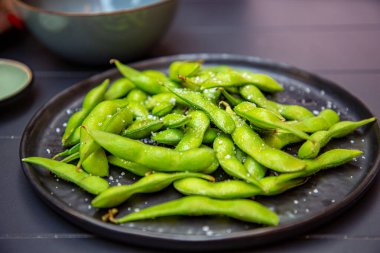 Pişmiş yeşil Edamame bir Japon restoranında siyah bir tabakta yatıyor..