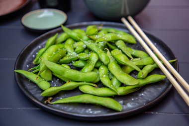 Pişmiş yeşil Edamame bir Japon restoranında siyah bir tabakta yatıyor..