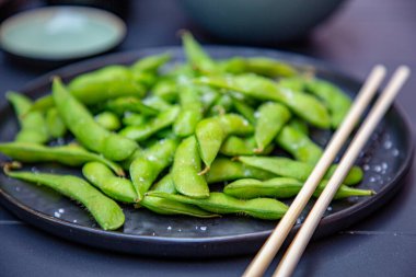Pişmiş yeşil Edamame bir Japon restoranında siyah bir tabakta yatıyor..