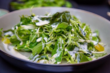 Koyu bir tabakta taze salata ve yoğurt sosu servis edilir.