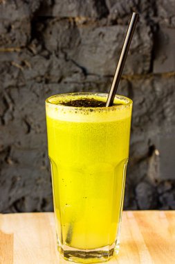 Bitki ve sebzelerden yapılmış yeşil smoothie büyük bir bardakta siyah taş bir duvara karşı.