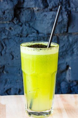 Bitki ve sebzelerden yapılmış yeşil smoothie büyük bir bardakta siyah taş bir duvara karşı.