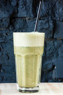 Bitki ve sebzelerden yapılmış yeşil smoothie büyük bir bardakta siyah taş bir duvara karşı.