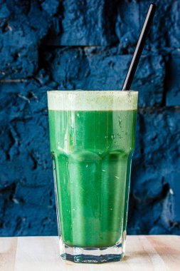 Bitki ve sebzelerden yapılmış yeşil smoothie büyük bir bardakta siyah taş bir duvara karşı.