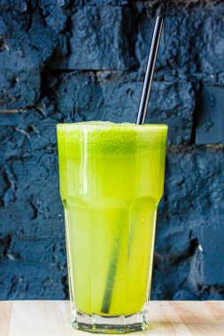 Bitki ve sebzelerden yapılmış yeşil smoothie büyük bir bardakta siyah taş bir duvara karşı.