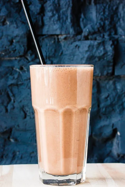Brown Smoothie or cocktail with coffee and yogurt in a large glass glass against a dark stone wall