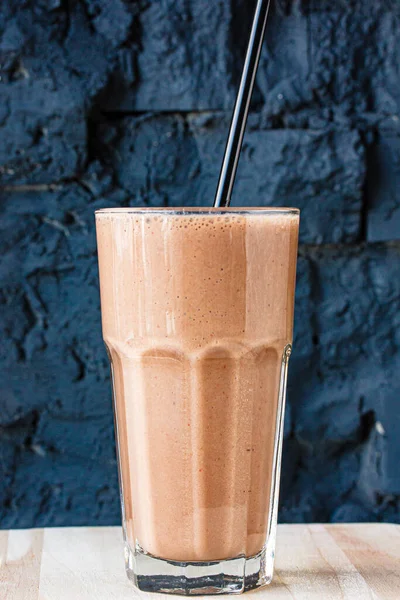 Brown Smoothie or cocktail with coffee and yogurt in a large glass glass against a dark stone wall