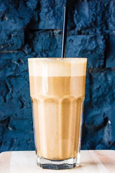 Brown Smoothie or cocktail with coffee and yogurt in a large glass glass against a dark stone wall