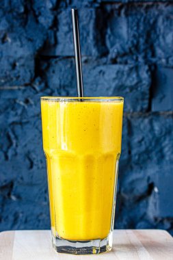 Sarı smoothie (portakal, mandarin) büyük cam bir fincanda siyah bir duvara karşı.