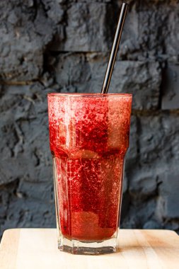 Büyük bir bardakta, koyu taştan bir duvara yaslanmış kırmızı meyve püresi.