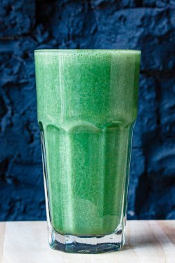 Bitki ve sebzelerden yapılmış yeşil smoothie büyük bir bardakta siyah taş bir duvara karşı.