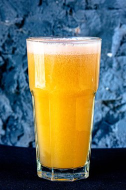 Sarı smoothie (portakal, mandarin) büyük cam bir fincanda siyah bir duvara karşı.