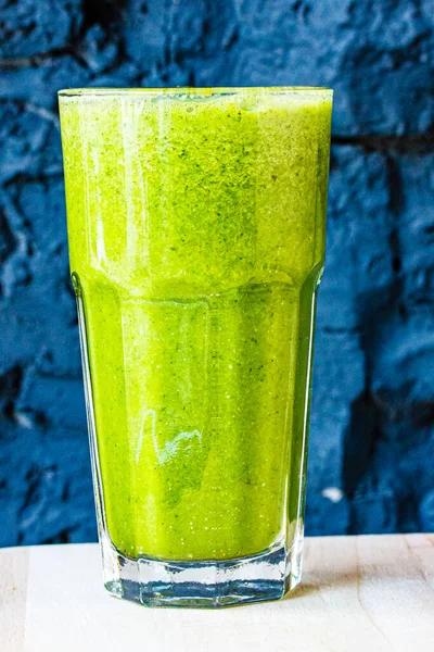 绿色的冰沙 由香草和蔬菜制成 装在一个大玻璃杯中 与深色的石墙相映成趣 — 图库照片
