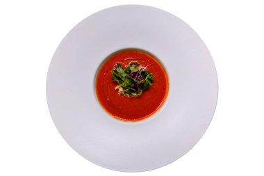 Gazpacho çorbasını beyaz tabağa dök ve roka ve diğer otlarla süsle..