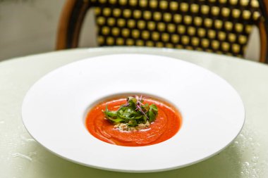 Gazpacho çorbasını beyaz tabağa dök ve roka ve diğer otlarla süsle..