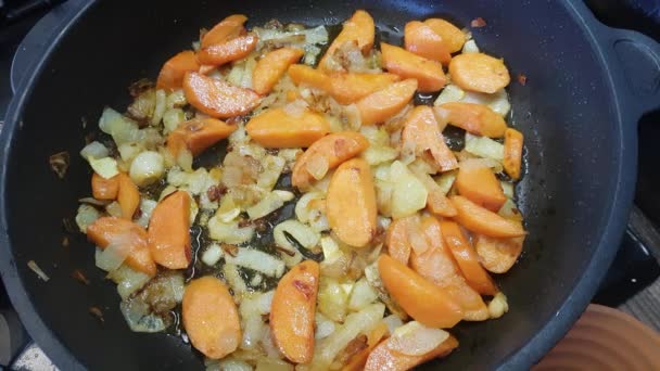 Cebule i marchewki smażone są na patelni. Kucharz miesza je łopatką. — Wideo stockowe