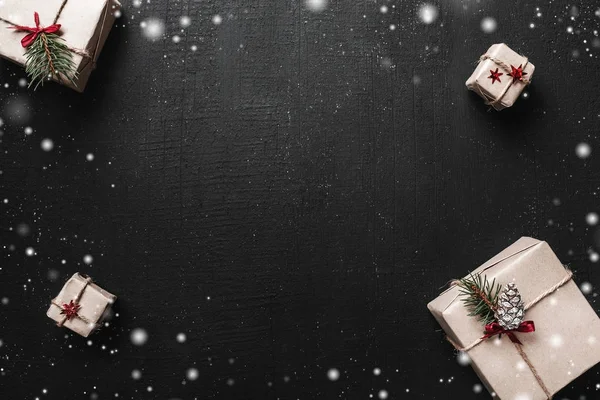 Geschenkdozen op zwarte achtergrond. Presenteert in ambacht met rood lint en sneeuwvlokken. Kerst en andere feestdagen concept. — Stockfoto
