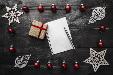 Üst, üst, görüntülemek üzerinden yukarıda kırmızı yaprak dökmeyen oyuncak, hediyeler, el yapımı kış figürinler, not defteri ve kalem ile yazma, tebrik metin için yer siyah arka plan üzerine.