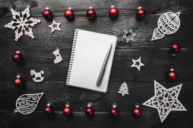 Üst, üst, yukarıdan, ahşap kış figürinler kırmızı oyuncaklar not defteri görüntülemek ve yazma, tebrik metin için yer ile siyah arka plan üzerine kalem.