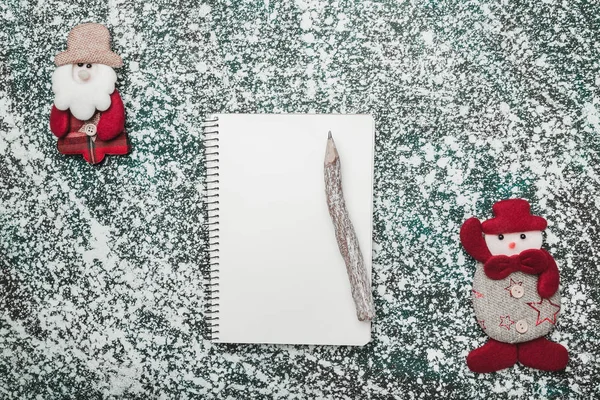 Upper, top, view from above of a notepad, wooden vintage pen, and handmade Santa and snowman toys on gray marble background, with space for text writing, greeting.