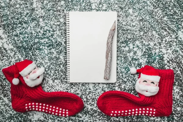 Upper, top, view from above of a notepad, wooden vintage pen, and handmade Santa socks on gray marble background, with space for text writing, greeting.