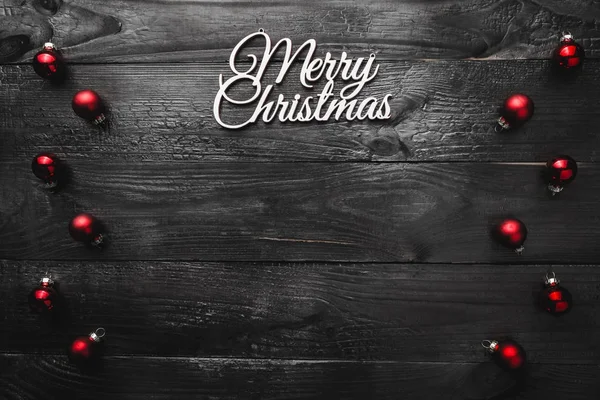 Üst, üst, görüntülemek üzerinden yukarıda, herdem yeşil kırmızı oyuncak ve yazma, tebrik metin için yer ile siyah ahşap zemin üzerine beyaz Merry Christmas yazıt.