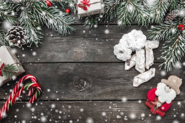 Çam dalları, Noel Baba el yapımı oyuncak, koniler, mevcut kutuları, çerezler ve şekerler, rustik koyu ahşap arka plan üzerinde yukarıdan görüntülenen, en yüksek kar tebrik kartı ile metin için yer ile Noel Tema