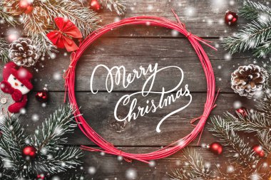Kırmızı dallar ve Merry Christmas daire xmas tema ile çam dalları, kırmızı yay ve küreler, koniler, el yapımı kardan adam oyuncak, yukarıdan izlendi rustik koyu ahşap arka plan, top, tebrik kartı üzerinde oturum