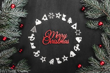 Üst, üst, görüntülemek yukarıdan, el yapımı ahşap oyuncaklar çemberi yuvarlak şekli, herdem yeşil dallarda siyah arka plan ve kırmızı mutlu Noeller yazıt, tebrik.
