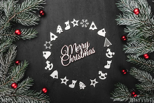 Üst, üst, görüntülemek yukarıdan, el yapımı ahşap oyuncaklar çemberi yuvarlak şekli, herdem yeşil dallarda siyah arka plan ve beyaz Merry Christmas yazıt, tebrik.