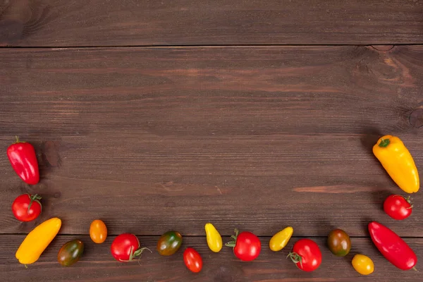 Various colorful cherry tomatoes and bell peppers on wooden background. Top view, flat lay with copy space