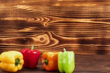 Ahşap arka planda yeşil, sarı, turuncu ve kırmızı dolma biber. Biyolojik yemek, taze sebze.