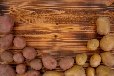 İşlenmemiş organik patateslerin değişik çeşitleri ve kahverengi ahşap arka planda kırmızı, sarı renkler. Taze sebzeler, üst görünüm, kopyalama alanı
