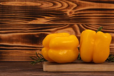Kesme tahtasında iki taze sarı dolma biber ve biberiye, ahşap arka plan. Taze sebzeler, organik yiyecekler.