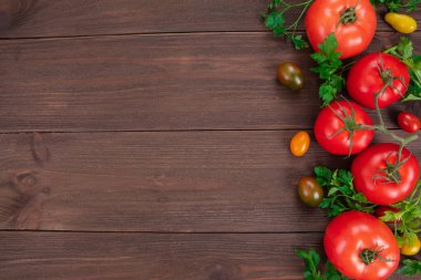 Çeri domatesleri, olgun kırmızı domatesler ve ahşap masada maydanoz yaprakları. Kopyalama alanı olan üst görünüm
