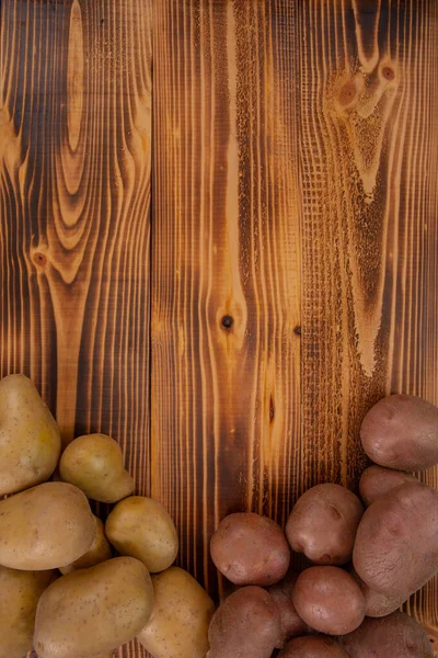 Heap of two types of potatoes on wooden rustic background. Bio vegetables, verical image with copy space