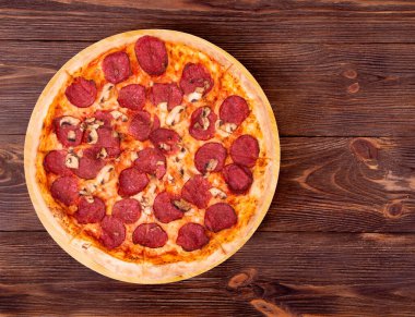Bambu tabanlı salamlı pizza, ahşap masa üstü manzaralı, metin için yer var.