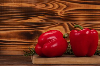 Kesme tahtasında kırmızı biber ve biberiye dalları, ahşap arka plan. Taze sebzeler, sağlıklı organik yiyecekler.