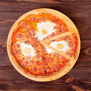 Biftek sosisli pizza, yumurta ve pastırma, ahşap bir tabakta dilimlenmiş, ahşap bir arka planda, üst manzara ve kopyalama alanı.