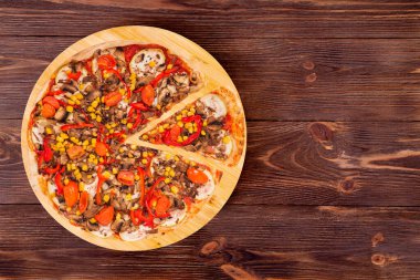 Mantarlı, mısırlı, kirazlı domatesli, kabaklı ve dolma biberli pizza, ahşap bir tabakta kesilmiş bir dilim, ahşap kırsal masa, üst manzara ve uzay kopyası.