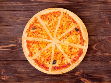 Dilimlenmiş pizza margherita mozzarella, bocconcini ve fesleğen yaprakları yuvarlak ahşap tabakta, ahşap arka planda, üst manzara