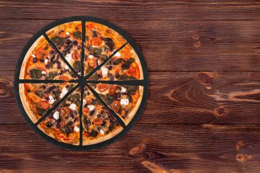 Kiraz domatesli dilimlenmiş pizza, ıspanak, mozzarella, feta, kalamata zeytin ve mantarlar tahta tabakta, üst görünüm ve metin için alan