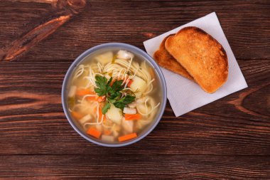 Erişteli leziz tavuk çorbası ve ahşap zemin üzerinde duran kağıt peçeteye iki dilim tost.