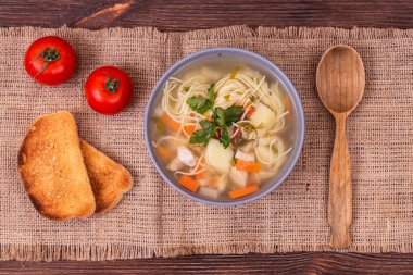 Sebzeli ev yapımı tavuk çorbası ve kasede taze maydanoz, ahşap kaşık, kiraz domatesleri ve desenli bir çuval bezi üzerine dilimler. Üst görünüm