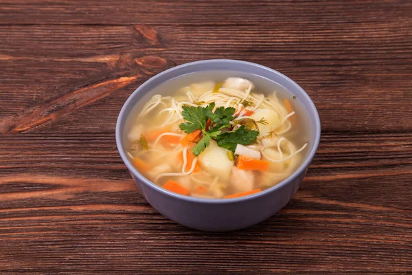 Kahverengi ahşap arka planda erişteli ev yapımı tavuk sebze çorbası.