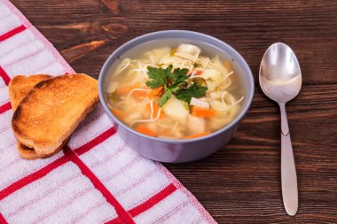 Kasede tavuk çorbası, bir kaşık, iki dilim tost ve kırsal ahşap bir masada peçete.