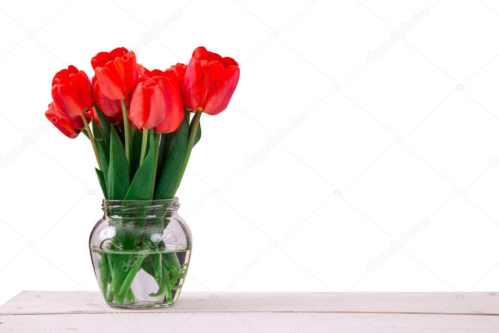 Bouquet of fresh red tulips in glass vase on wooden table, isolated on white background