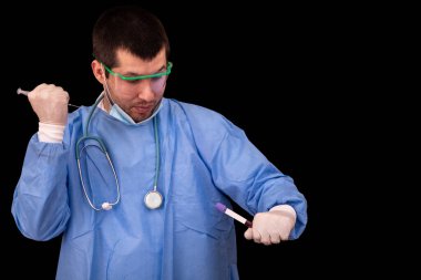 Coronavirus 'un kirlenmesinden korunan tıbbi adam bir deney yapıyor, bir elinde şırınga, diğerinde üzerinde yazı için yeri olan bir test tüpü tutuyor.